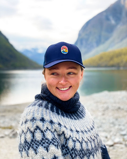 Trucker Cap Navy – smilende kvinne i strikkegenser med capsen ved en innsjø