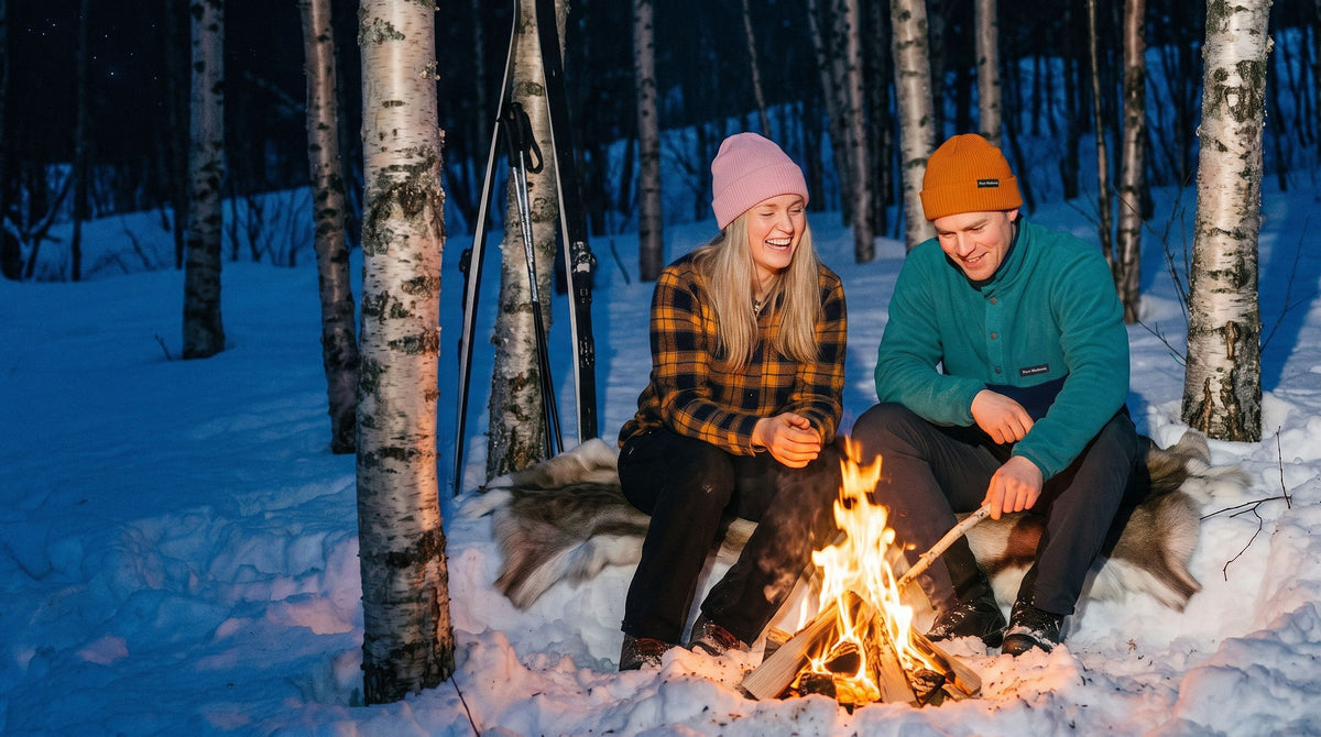 To venner ler rundt et bål i en snødekt bjørkeskog, i Pure Madness merinolue og fleece