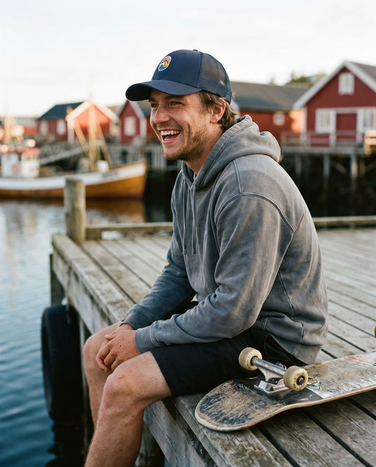 Trucker Cap Navy – leende mann med skateboard sitter på brygga i en havn