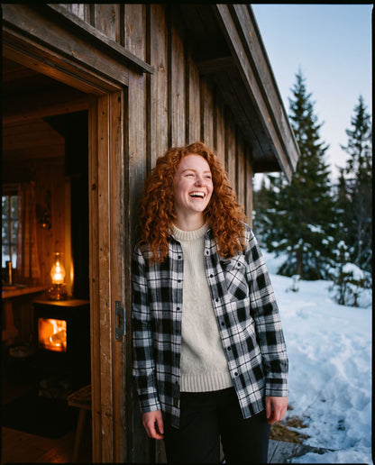 Voss Flannel Shirt Whiteout – leende kvinne i døra på en hytte med vedovnen fyrt opp