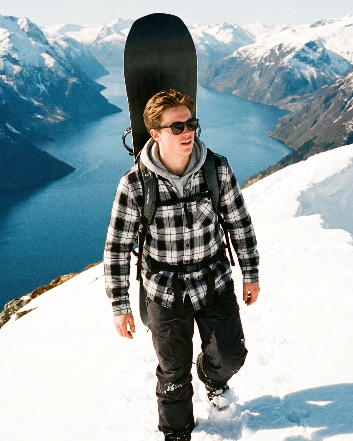 Voss Flannel Shirt Whiteout – mann går opp en snøkam med snowboard på sekken over fjorden