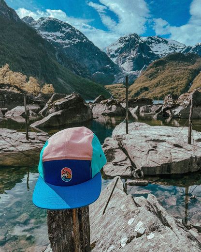 5 Panel Cap Ocean Sunset – caps i rosa, marineblått og turkis på en stolpe ved et fjellvann