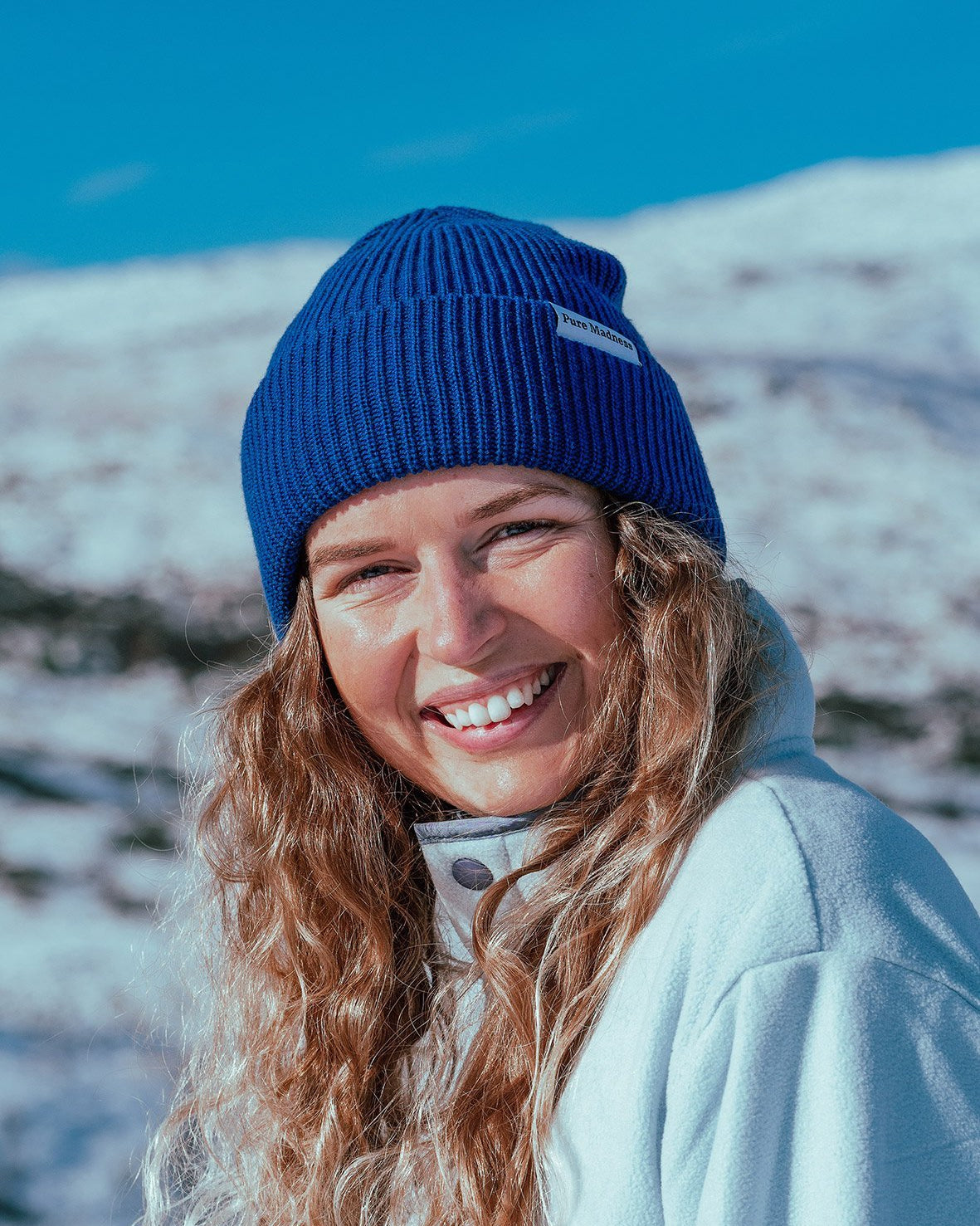 Blue Captain Merino Beanie – smilende kvinne med koboltblå lue foran snødekt fjell
