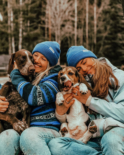 Blue Captain Merino Beanie – to kvinner med blå luer koser med to hunder
