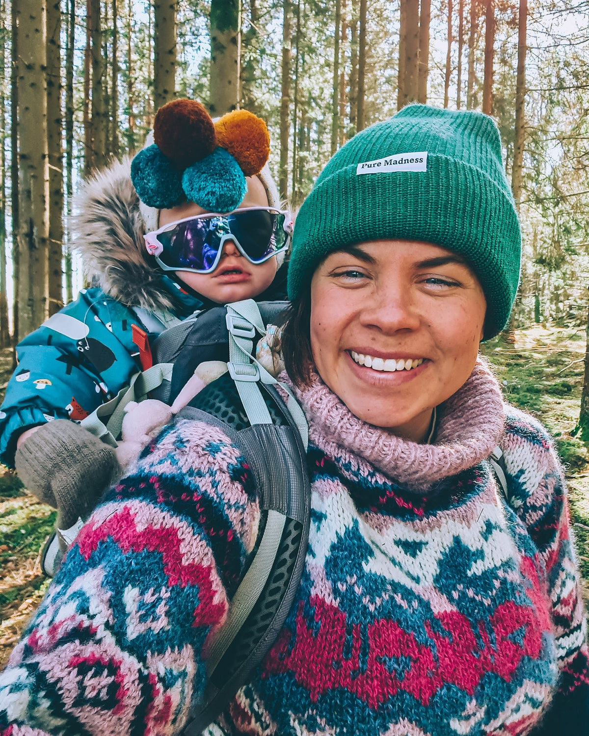 Green Captain Merino Beanie – smilende kvinne med grønn lue og barn i bæremeis i skogen