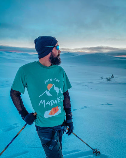 Join the Madness Teal Tee – mann med skistaver i turkis t-skjorte på snødekt vidde