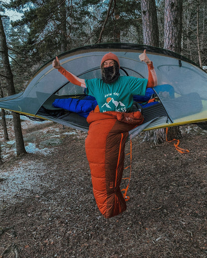 Join the Madness Teal Tee – person i hengekøyetelt med t-skjorta og sovepose, tomlene opp