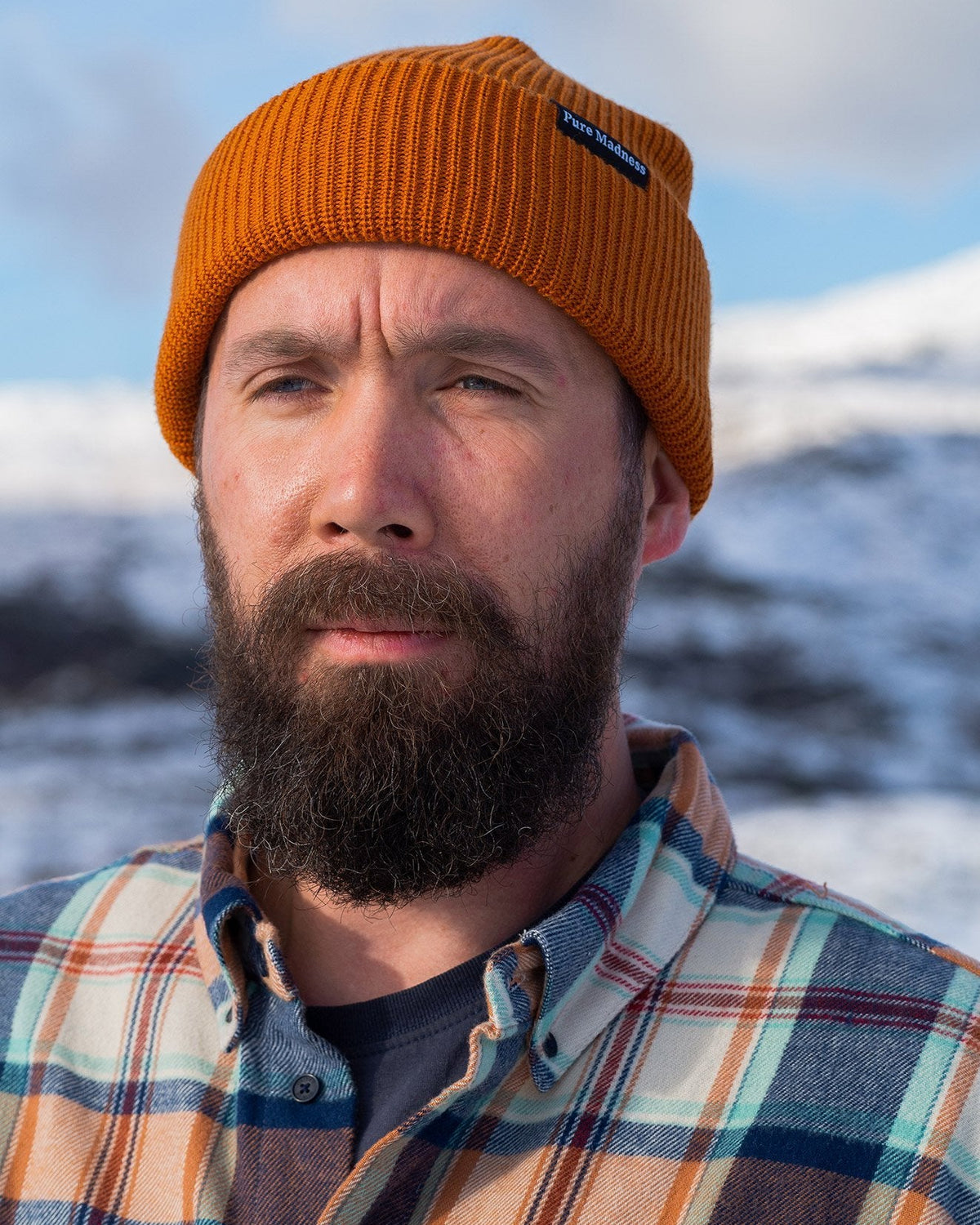 Orange Captain Merino Beanie – mann med skjegg og oransje lue foran snødekte fjell